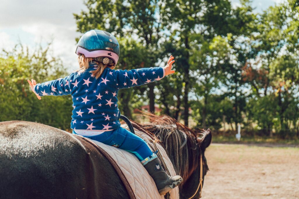 pexels photo 1364073 1364073 A child confidently rides a horse outdoors, wearing a helmet and star-patterned jacket.